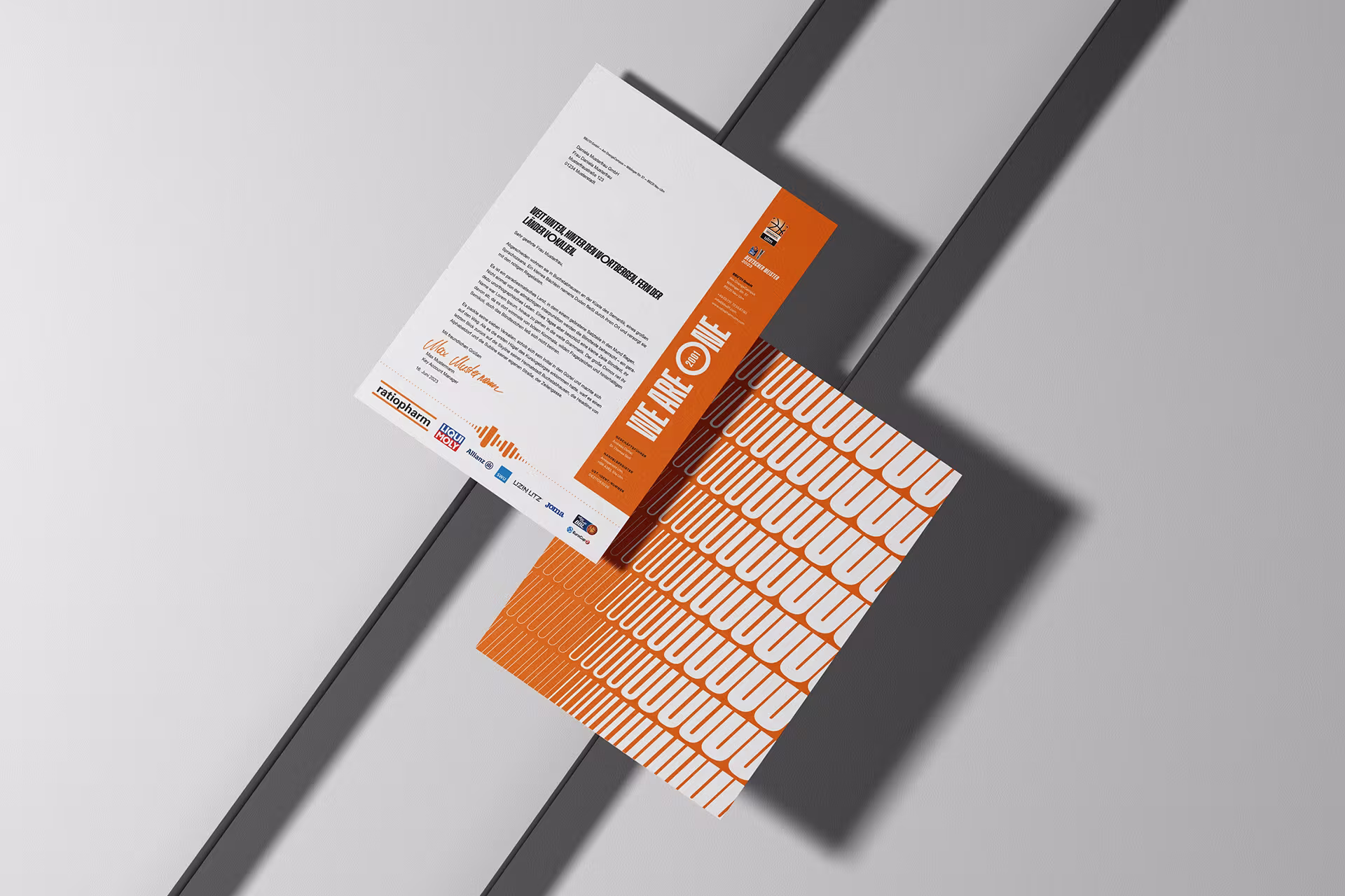Briefbogen mit orangefarbener Seitenleiste und „We Are One“-Slogan sowie Rückseite mit dynamischem UUU-Muster in Weiß auf Orange.