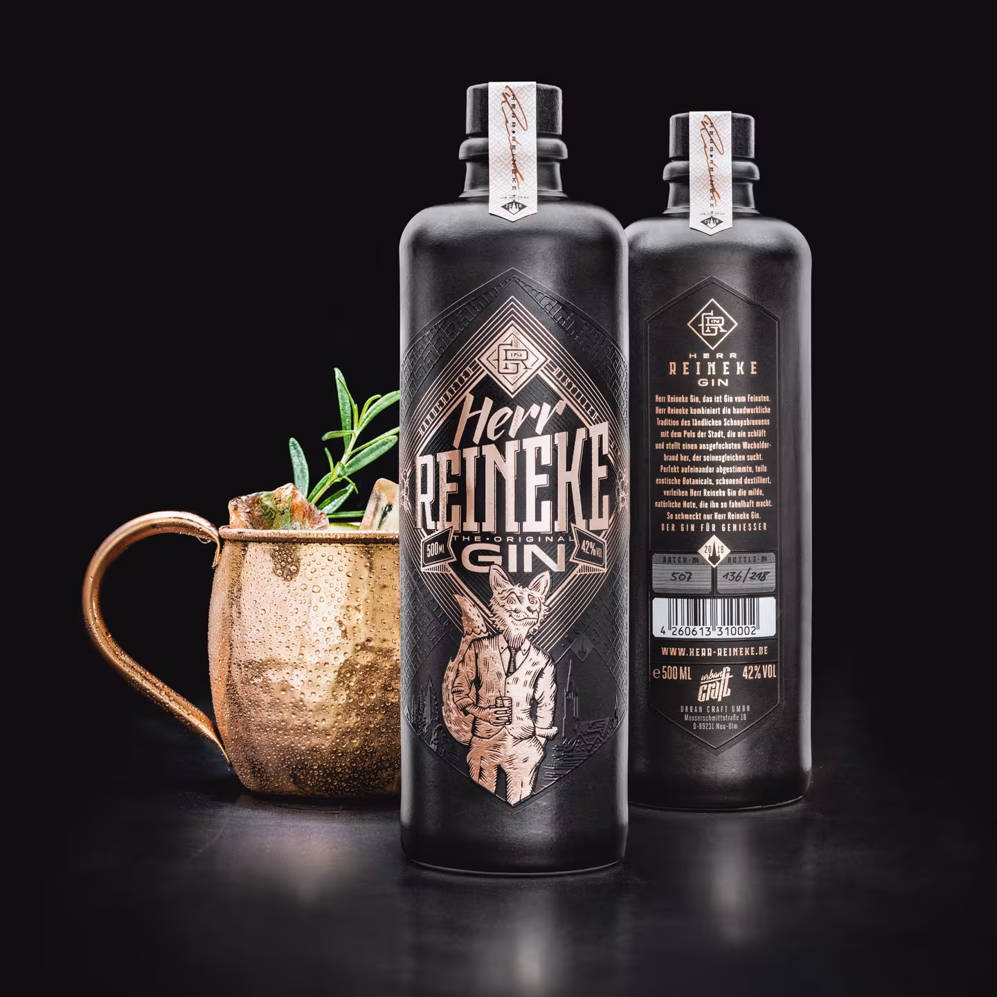 Vorder- und Rückseite der Herr Reineke Gin-Flasche neben einem Kupferbecher mit Rosmarin-Garnitur – hochwertige Inszenierung von Etikett und Textur