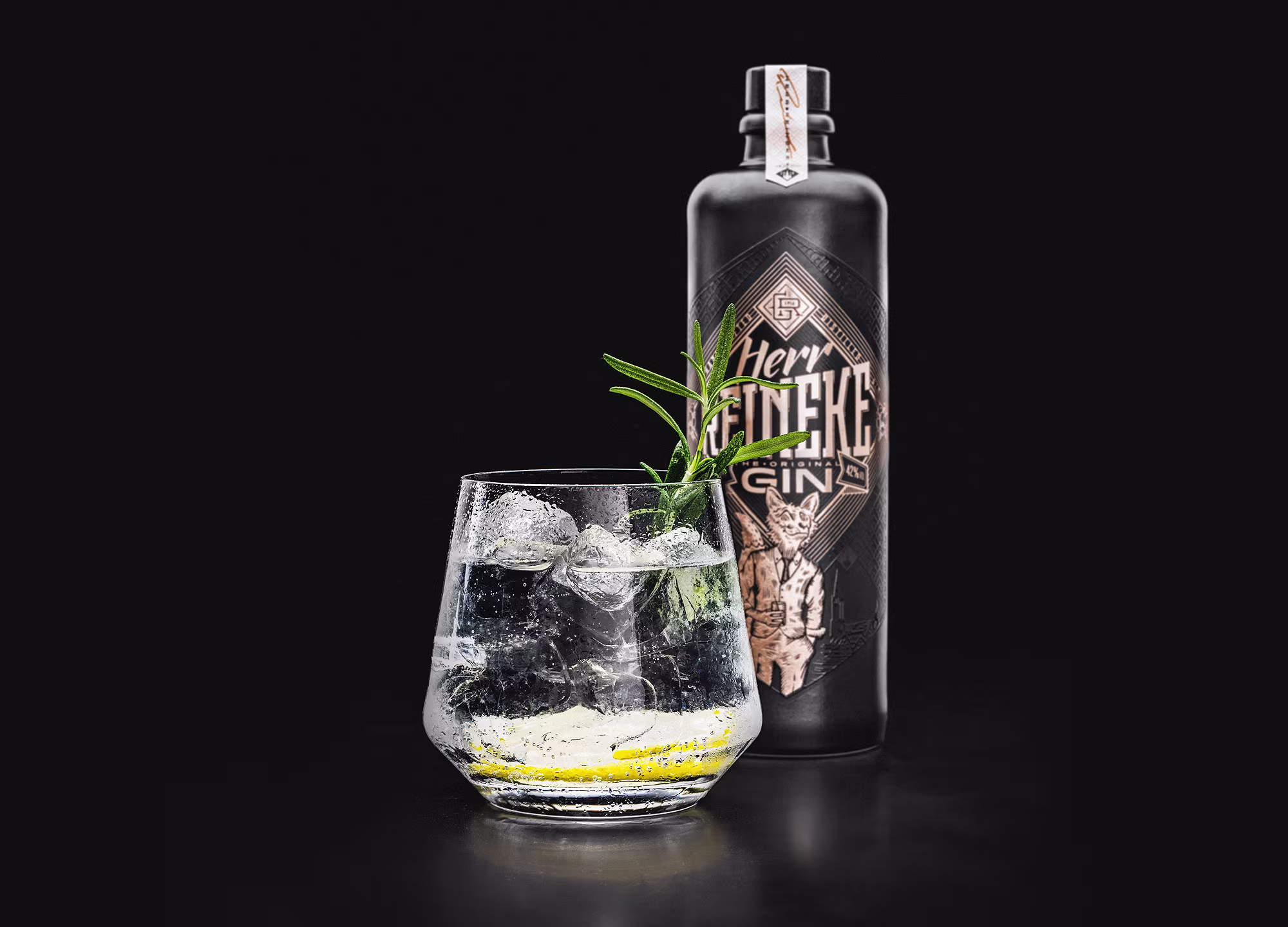 Gin & Tonic im Glas mit Eis, Zitrone und Rosmarin vor der mattschwarzen Herr Reineke Gin-Flasche